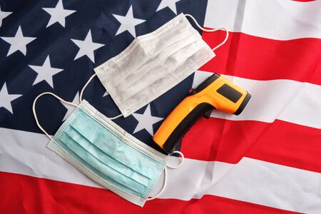 Used protective face masks and non-contact infrared thermometer on american flag background. Covid-19 quarantine. Flat lay, top viewの写真素材