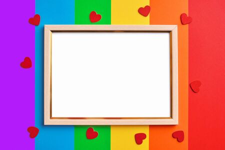 wooden frame with blank white copy space on multicolored rainbow flag background and little red hearts. Pride day concept, flat layの写真素材