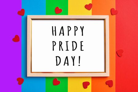 wooden frame with blank white copy space on multicolored rainbow flag background and little red hearts. Pride day concept, flat layの写真素材