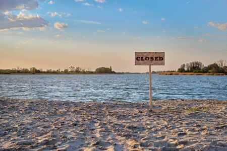 Signpost with inscription closed along the abandoned sand beach river. Contaminated water, quarantine, virus outbreak, access fee limitation concept.の写真素材