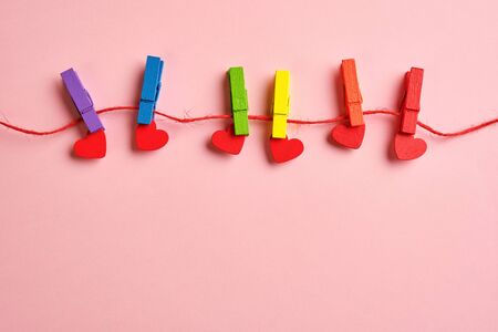 rainbow colored wooden clothespins with clamped red hearts on pink background. Pride day concept, flat lay, copy spaceの写真素材