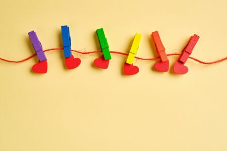 rainbow colored wooden clothespins with clamped red hearts on yellow background. Pride day concept, flat lay, copy spaceの写真素材