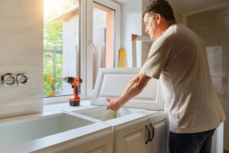 Middle-aged Caucasian man holds kitchen cabinet door , preparing for the process of custom installation in his own house. Quarantine activity, repair conceptの写真素材