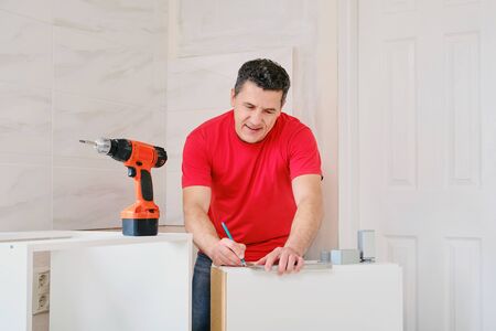 man makes markings with pencil and ruler when assembling kitchen furnitureの写真素材
