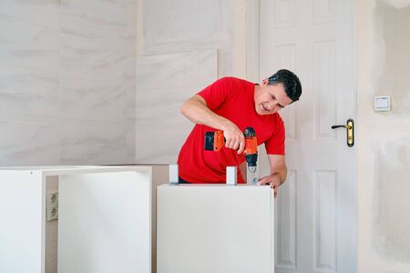 middle aged white man screwed the cabinet legs into wooden furniture with cordless screwdriver.の写真素材