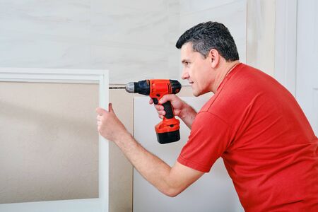 middle aged white man drilling hole into wooden furniture with cordless screwdriver.の写真素材