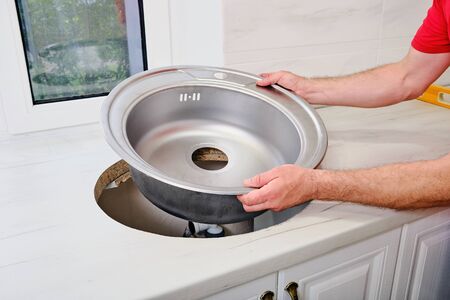 mans hands installs new round single stainless steel sink into a cut-out hole in the kitchen worktop.の写真素材