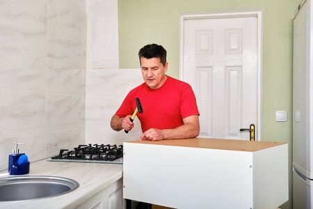 middle aged caucasian man assembling kitchen cabinet with hammer and nails.の写真素材