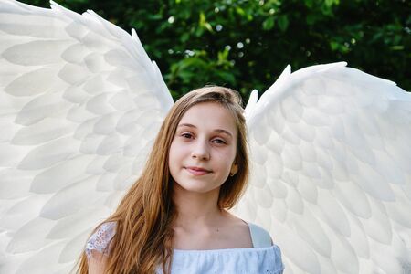 cute white teenage girl with angel wings and white dress posing outdoorsの写真素材