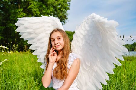 cute white teenage girl with angel wings and white dress posing outdoorsの写真素材