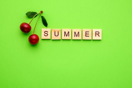 Two cherries with leaves and text summer from wooden blocks on green background.の写真素材