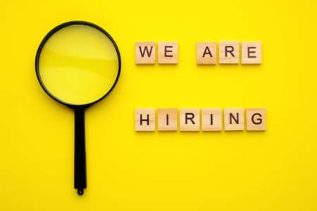 wooden block lettering we are hiring and magnifying glass on yellow background.の写真素材