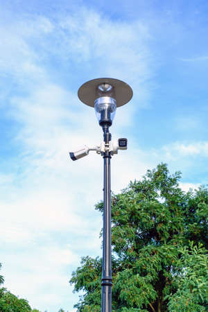 Two white surveillance cameras on the metal lamp post on blue sky background.の写真素材