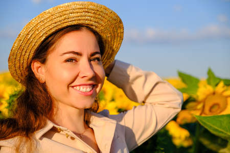 close up portrait of a smiling woman in straw hat in blooming sunflower field at sunrise.の写真素材