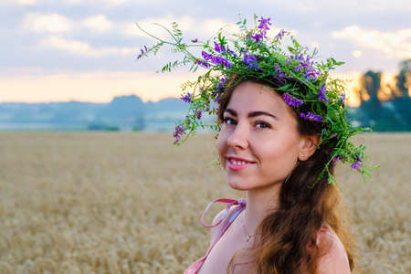 Happy smiling girl with long hair with a flower wreath on head in wheat field at sunrise.の写真素材