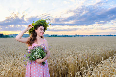 Happy smiling girl with long hair with a flower wreath on head holds a wild flower bouquetの写真素材