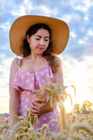 Pretty young girl with long hair holds golden stalks of wheat in field at sunrise.の写真素材