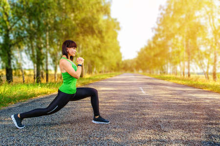 Young caucasian woman stretching legs before jogging on asphalt road in countryside, warming up for muscles. Empty space for textの写真素材