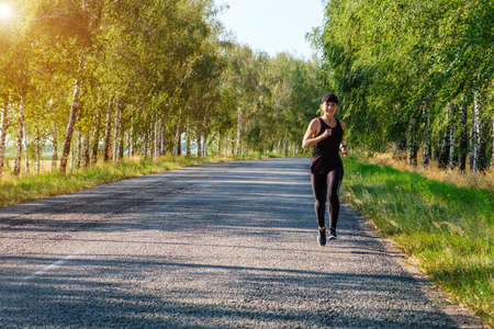young white fitness woman runs on country road, front view. Workout, fitness, marathon concept. Copy space for textの写真素材