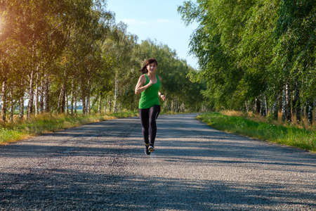 young white fitness woman runs on country road, front view. Workout, fitness, marathon concept.の写真素材