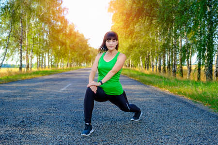 Young caucasian woman stretching legs before jogging on asphalt road in countryside, warming up for muscles.の写真素材