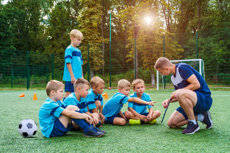 Young coach teaches little children the strategy of playing on football field.の写真素材
