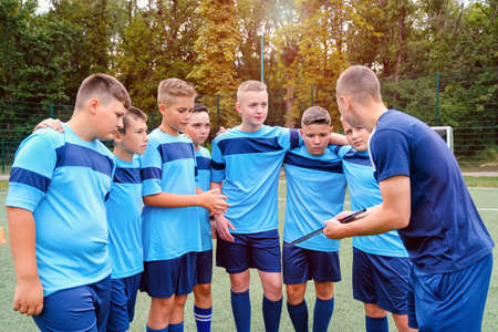 Kids in football uniform embraces and listening to explain of coach.の写真素材
