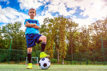 Full length portrait of a kid in sportswear posing with a soccer ball outdoorsの写真素材