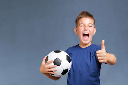 Handsome screaming caucasian fan boy holds soccer ball and gesturing thumbs upの写真素材