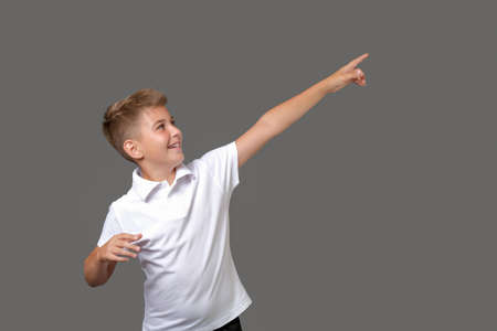 young boy wearing white t-shirt pointing away over with finger isolated on grayの写真素材