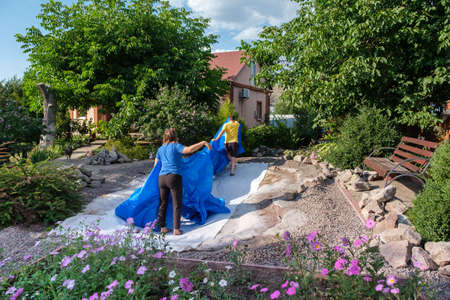 Family lays a blue HDPE plastic sheet on the ground to set up a fish pondの写真素材