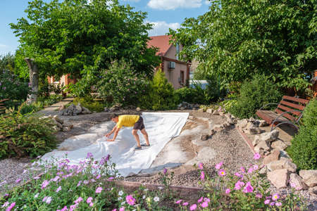 man roll out a roll of white non-woven geotextile fabric before set up fish pondの写真素材