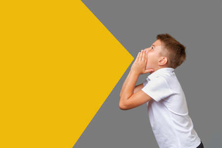 Boy screams with hands folded as megaphone isolated on gray-yellow backgroundの写真素材