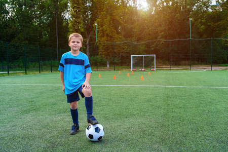 Full length portrait of a kid in sportswear posing with a soccer ball on football field outdoorsの写真素材