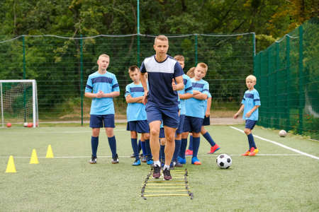 Young caucasian coach showing the players exercises to improve their game skills. Children football training conceptの写真素材