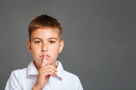 kid asking to be quiet with finger on lips isolated on grey background. silence, conspiracy and...