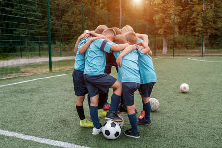 Children soccer team and coach hugs each other on football field before match outdoors at summerの写真素材
