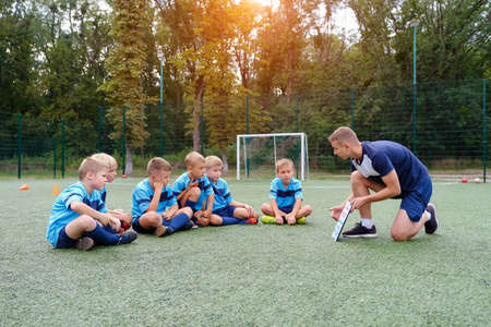 Young coach with clipboard teaches children strategy playing on football field.の写真素材