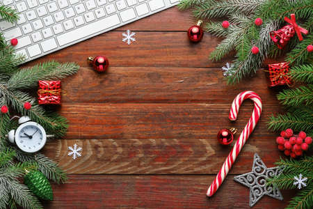 Christmas background and decoration with fir branches, computer keyboard, alarm clock, gift boxes and candy on old wooden board with copy space.の写真素材