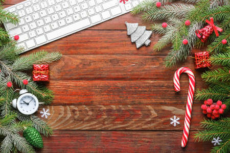 Christmas background and decoration with fir spruces, computer keyboard, alarm clock, gift boxes, toys and candy on old wooden board with copy space. Top view, flatlayの写真素材