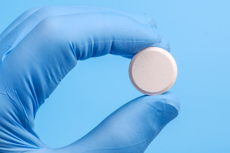 Big white tablet in hand wearing medical glove on blue background. Close Up viewの写真素材