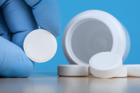 Hand in blue medical gloves holds big white pill near empty bottle of medical prescription tablets. Close up viewの写真素材