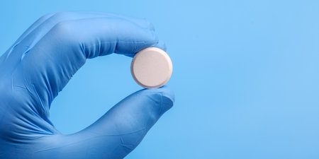 Big white tablet in hand wearing medical glove on blue background. Close Up view, copy spaceの写真素材