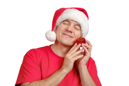 Satisfied middle-aged caucasian man in Santa hat receive small Christmas gift, holds near his face and smiling with closed eyes isolated on white background.の写真素材