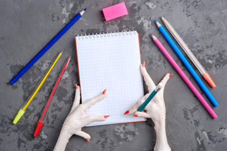Painted chicken paw holds a pencil over a sheet of white paper for writing. Chicken scratch and National Handwriting Day celebration concept, top view, copy spaceの写真素材