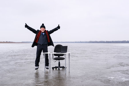 Senior smiling bearded businessman in suit stands with outstretched hands at a table in the middle of a frozen lake in winter. Copy space for textの写真素材