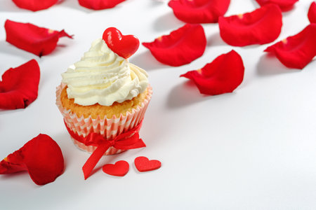 rose petals, two wooden hearts and valentines cupcake with heart shaped caramel candy on white background. High quality photoの写真素材