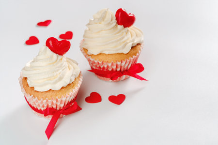 Two valentines cupcakes with hearts shaped caramel candy tied red ribbons on white background. High quality photo, copy space for textの写真素材