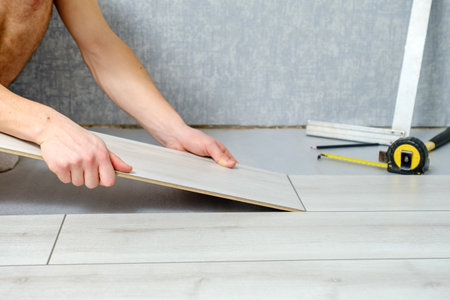 male hands is laying wooden panel of laminate floor indoors close-up. Laminate flooring, copy spaceの写真素材
