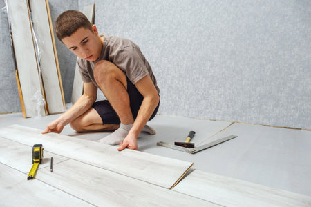 Young man is laying wooden panel of laminate floor indoors. Laminate flooring, copy spaceの写真素材